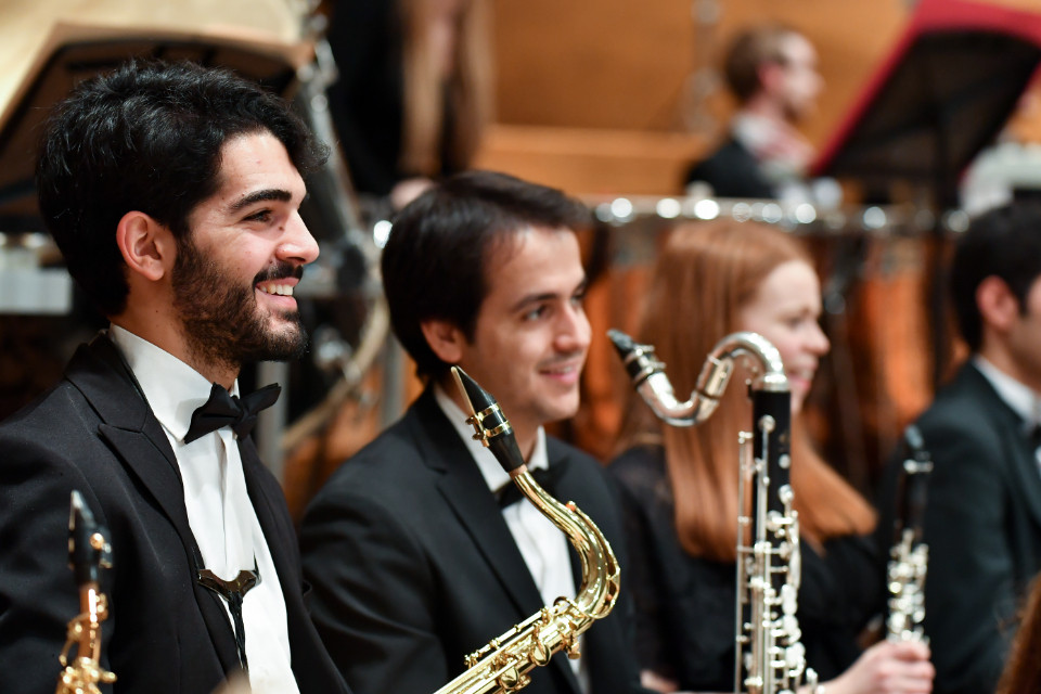 Two male students, wearing smart outfits, holding an alto saxophone and bass clarinet, smiling.